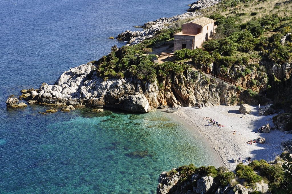 petite crique sicilienne avec plage de sable blanc, eaux turquoise et maisons côtières