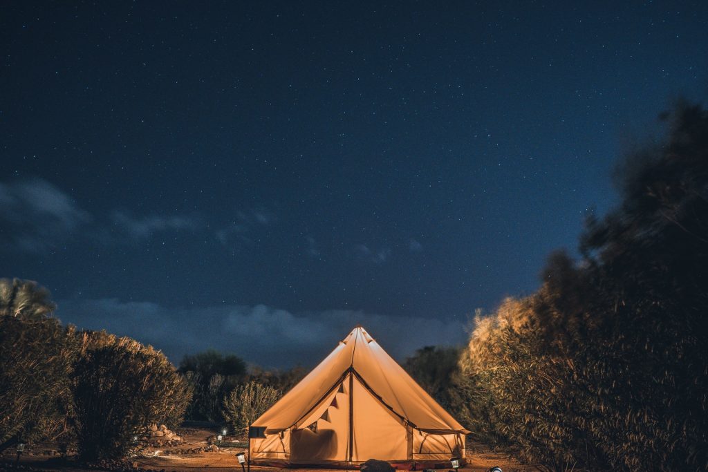 tente de glamping orange illuminée sous ciel étoilé en camping de nuit