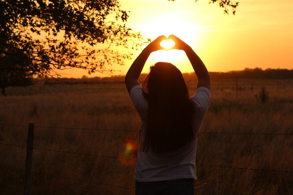 femme formant un cœur avec ses mains au coucher de soleil en France