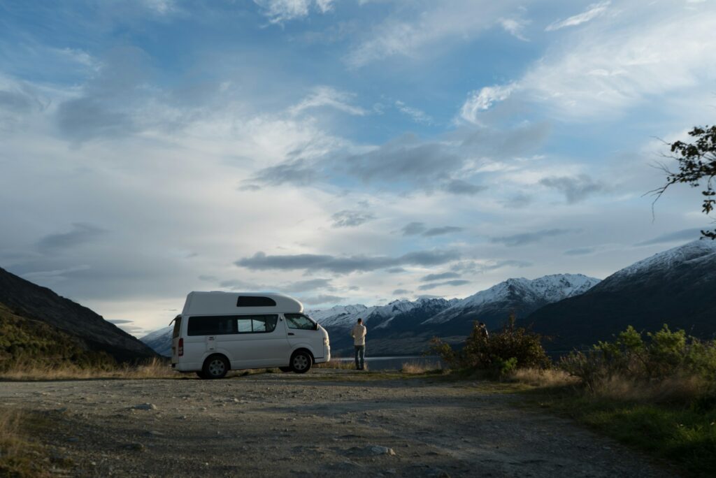 van aménagé blanc stationné dans une vallée de montagne enneigée avec voyageur
