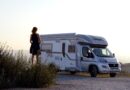 woman in black dress standing beside white and blue rv trailer during daytime