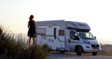 woman in black dress standing beside white and blue rv trailer during daytime