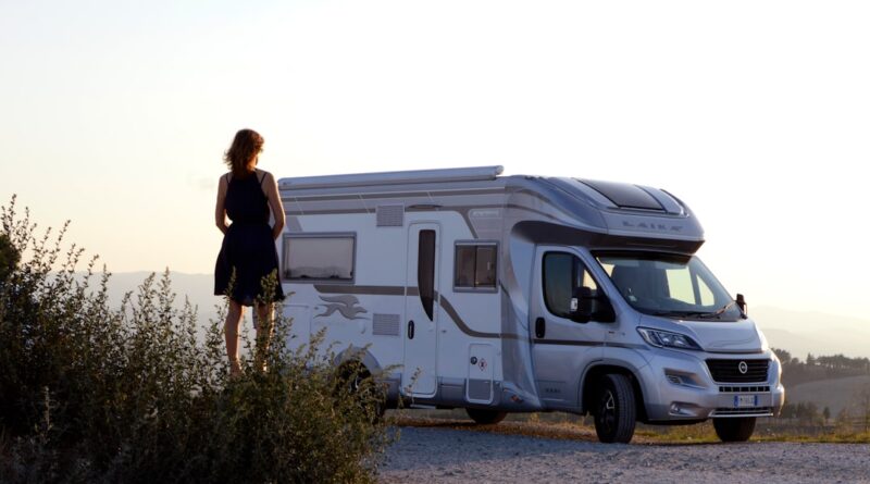 woman in black dress standing beside white and blue rv trailer during daytime